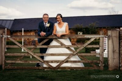 Wedding couple posing behind farm gate in countryside.