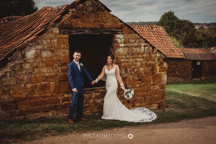Couple in wedding attire by old stone building.