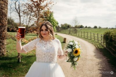 Bride holding pint and bouquet outdoors at countryside wedding.