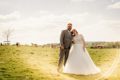 Wedding couple posing in sunny field with sheep.