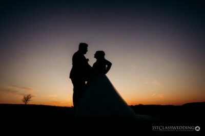 Couple's silhouette against sunset at wedding.