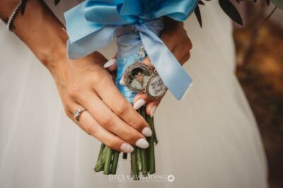 Bride holding bouquet with photo charm and blue ribbon.