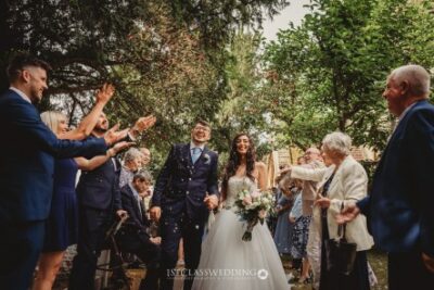 Bride and groom smiling with guests throwing confetti outside.