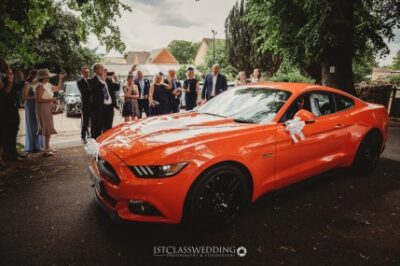 Red wedding car and guests at ceremony venue.