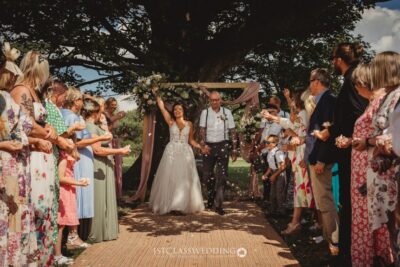 Joyful outdoor wedding ceremony with guests throwing confetti.