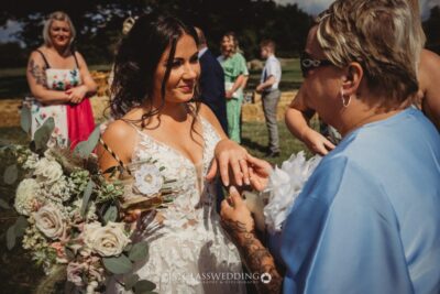 Bride in lace dress with bouquet at sunny outdoor wedding.