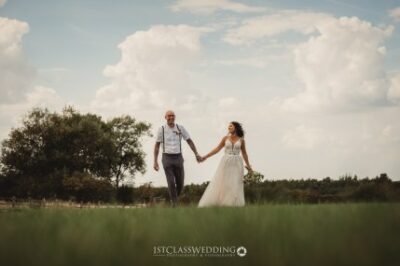 Couple holding hands in field on wedding day.