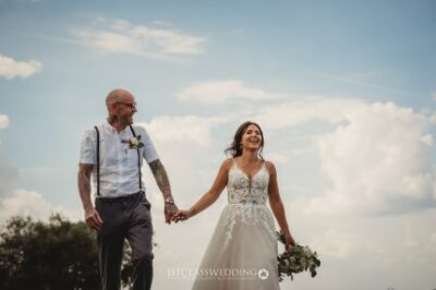 Bride and groom holding hands under blue sky.