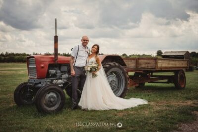 Bride and groom posing with vintage tractor in field.