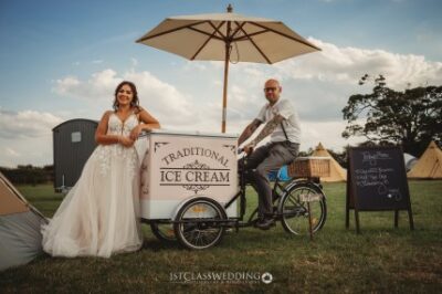 Bride and groom with vintage ice cream cart at wedding.