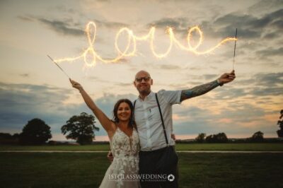 Couple with sparklers forming "love" at twilight wedding.