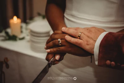 Couple's hands with wedding rings cutting cake.