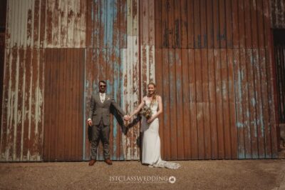 Couple posing for wedding photo by rustic barn wall.