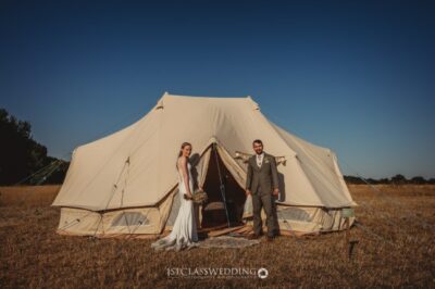 Bride and groom outside canvas tent in a field.
