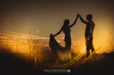 Couple silhouette at sunset in fields.