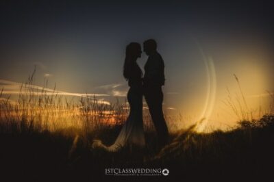 Couple silhouetted against sunset in a field.