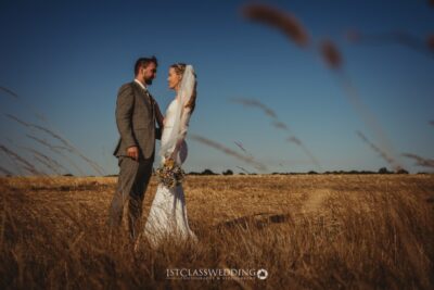 Couple in wedding attire standing in a field.