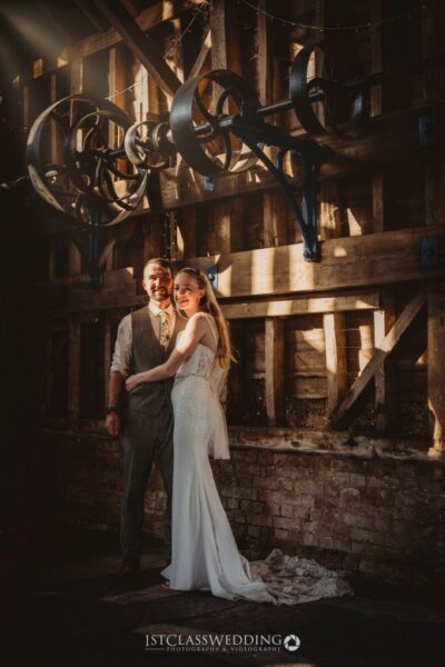 Couple posing in vintage wedding attire, rustic backdrop.