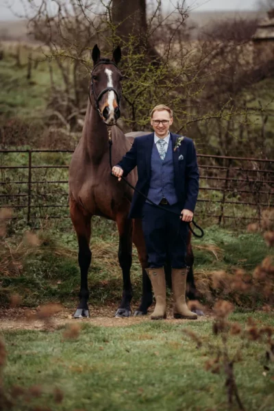 Man in suit with horse in countryside.