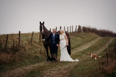 Bride, groom with horse and dogs in countryside wedding.