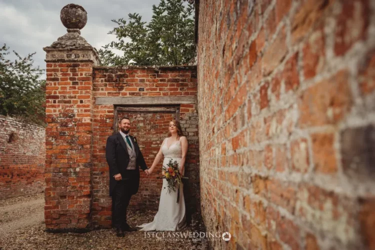 Bride and groom posing by historic brick wall.