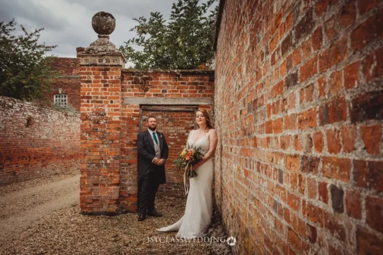 Bride and groom posing by historic brick wall.