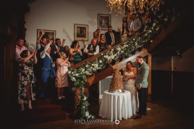 Couple cutting wedding cake with guests applauding.