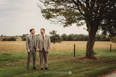 Grooms holding hands in rustic countryside wedding setting.