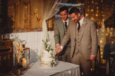 Grooms cutting wedding cake at rustic venue.