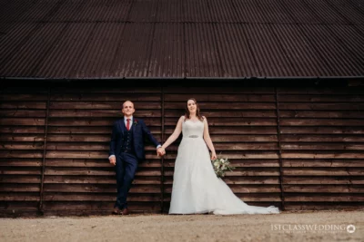 Bride and groom holding hands by wooden barn.
