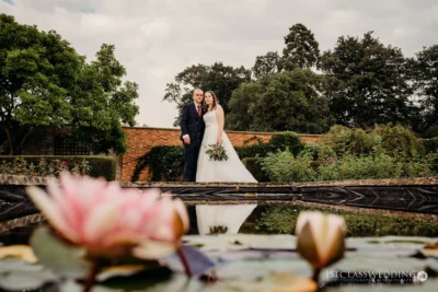 Couple posing by pond with water lilies at garden venue.