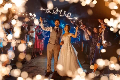 Wedding couple with sparklers and 'love' sign at night.