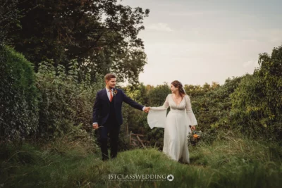Bride and groom holding hands in countryside.