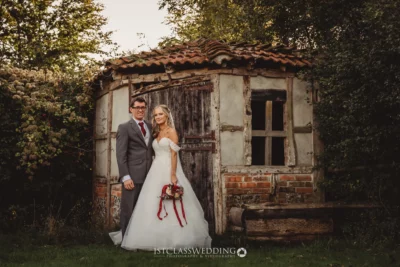 Couple posing in wedding attire by rustic building.