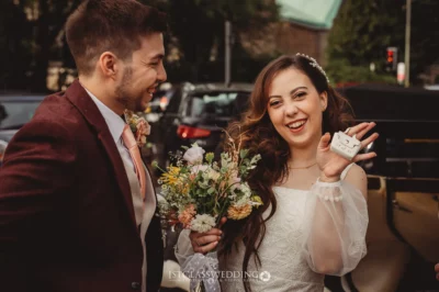 Joyful newlyweds with bouquet and rings outdoors.