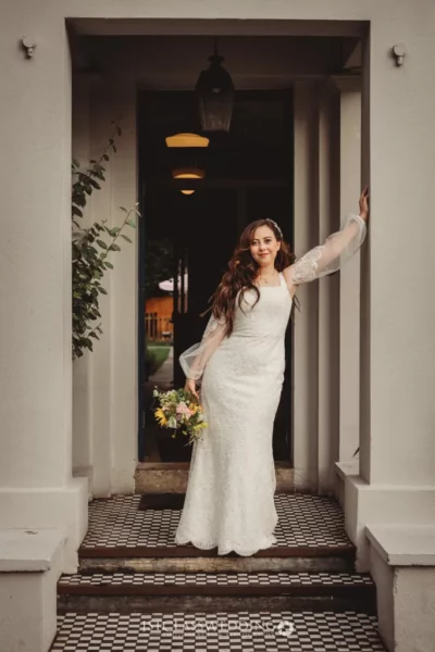 Bride on steps with bouquet, elegant dress.