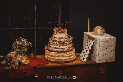 Naked wedding cake with berries and gift box.