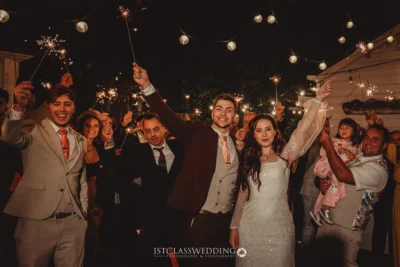 Joyful wedding guests with sparklers at night celebration.