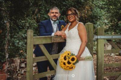 Couple with sunflower bouquet at rustic wedding.