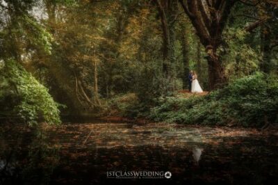 Wedding couple standing by forest pond in autumn.