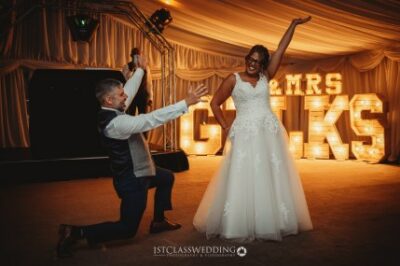 Joyful wedding dance under illuminated "Mr & Mrs" sign.