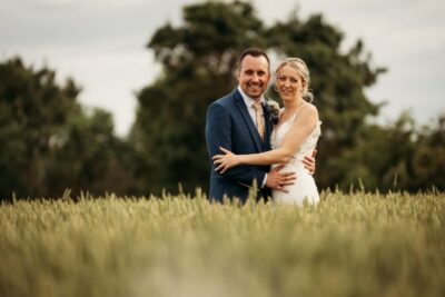 Happy couple posing in field on wedding day.