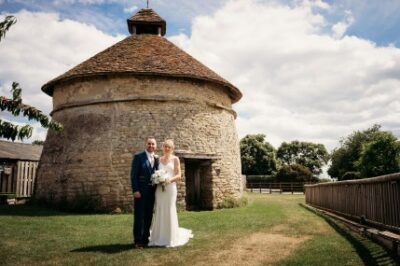 Wedding couple standing by historic stone building under blue sky.
