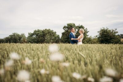 Couple embracing in a sunny field with trees.