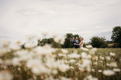 Couple embracing in a flower field, cloudy sky.