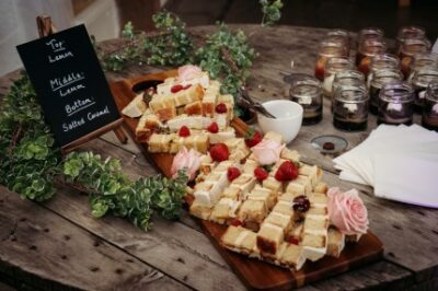 Afternoon tea sandwiches and desserts display on wooden board.