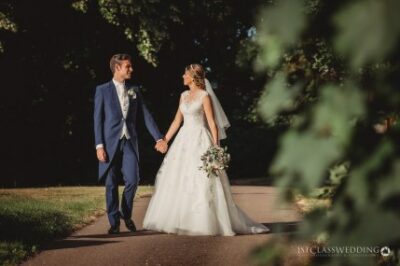 Bride and groom walking hand in hand in park.