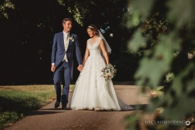 Bride and groom walking together on a sunlit path.