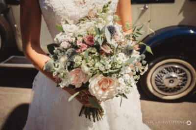 Bride holding bouquet with vintage car background.