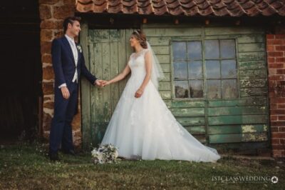 Bride and groom holding hands by rustic barn door.